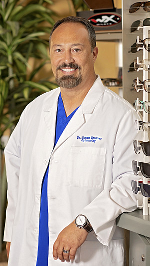 Angelo State alum Dr. J. Warren Brasher standing next to a rack of glasses and sunglasses