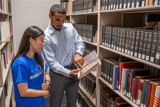 Students standing next to a bookshelf looking at a book together.