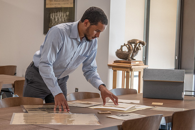 Student standing at a table looking at historical documents.