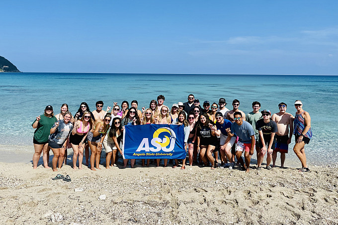 Students on a beach in Greece holding up an ASU flag