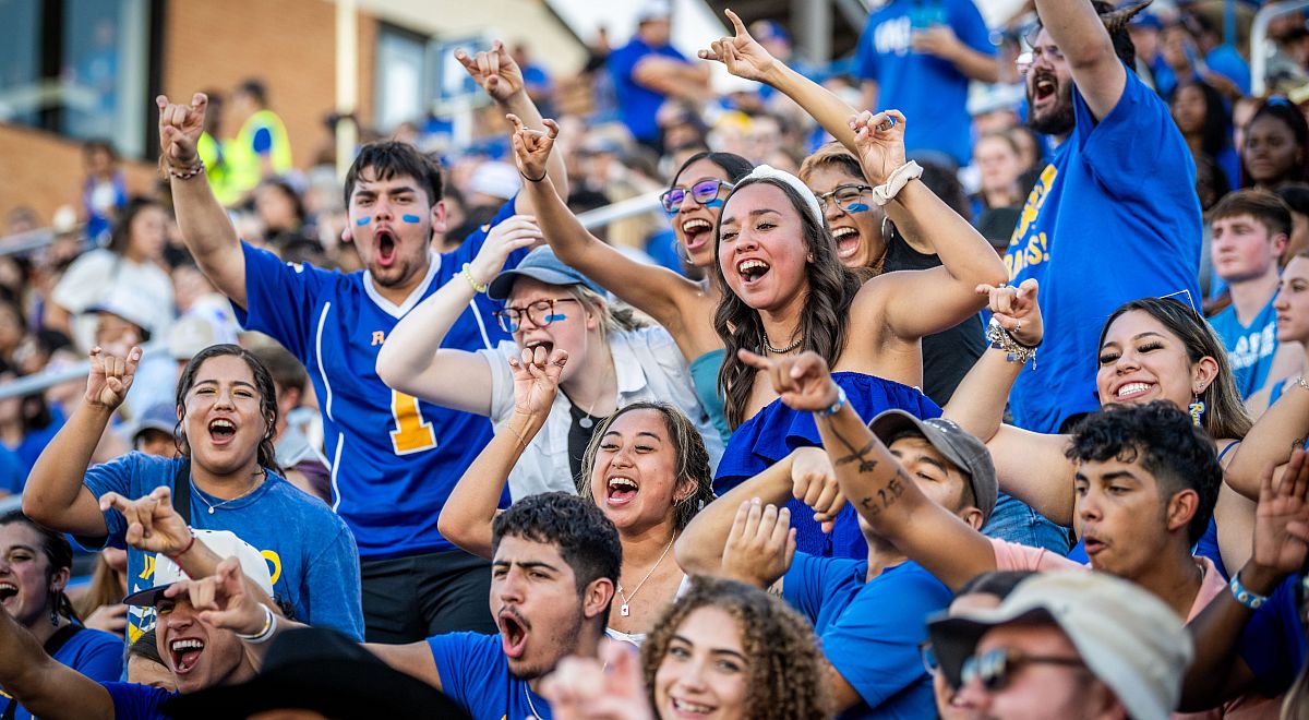 Students holding up the ram hand and cheering in the football stands.