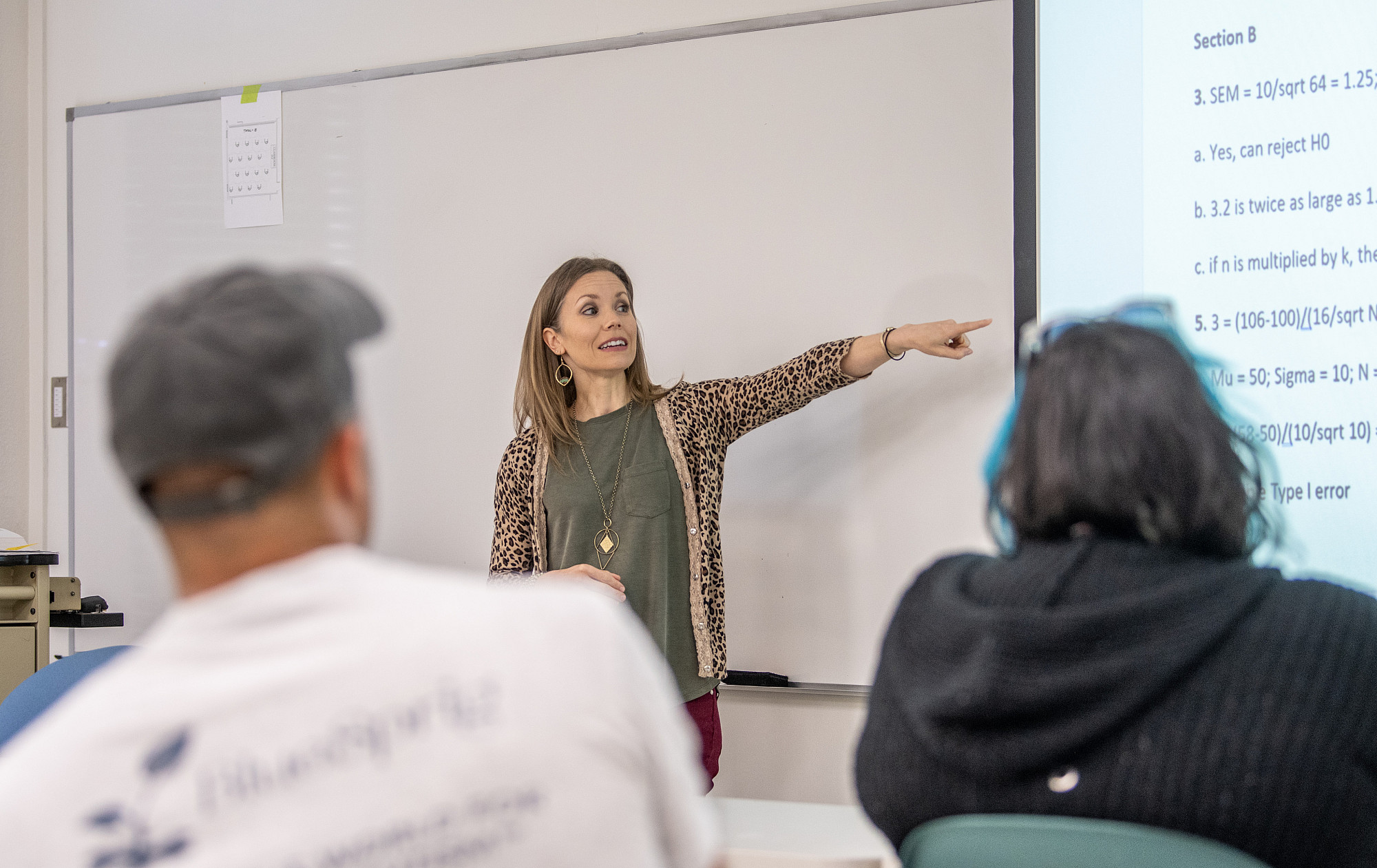 Professor points to the screen while students in the foreground listen.