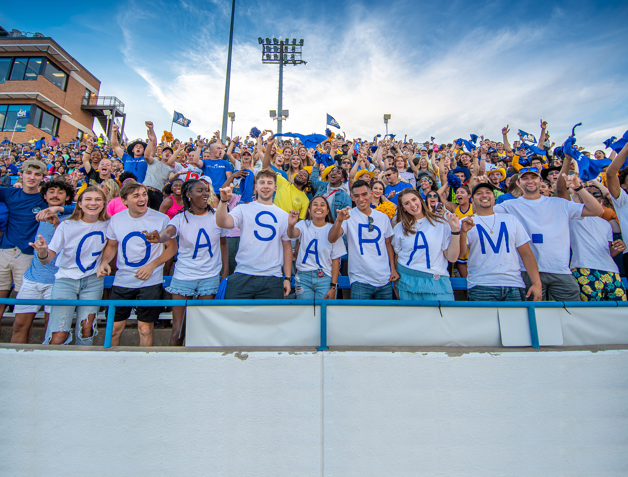 Students cheering in a stadium wearing shirts that spell Go As A Ram.