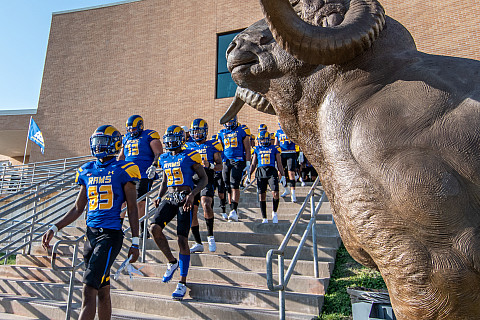 Rams Football team exiting the Junell Center stairs and coming onto the field with a Ram statue in the left corner