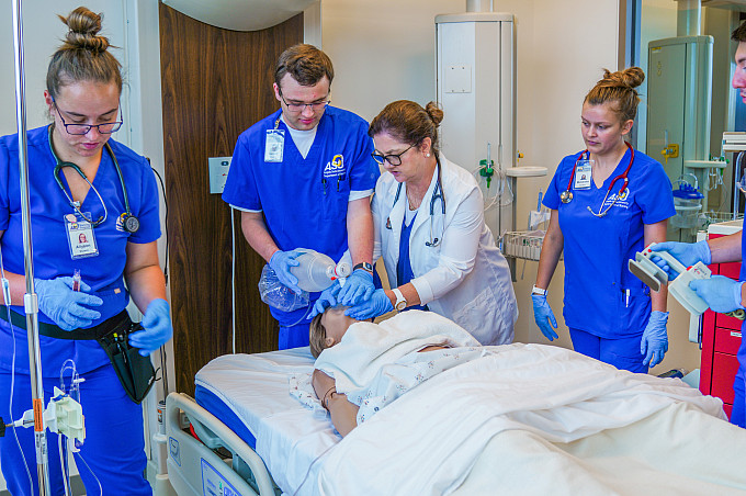 Nursing professor showing students how to perform CPR on a manikin.