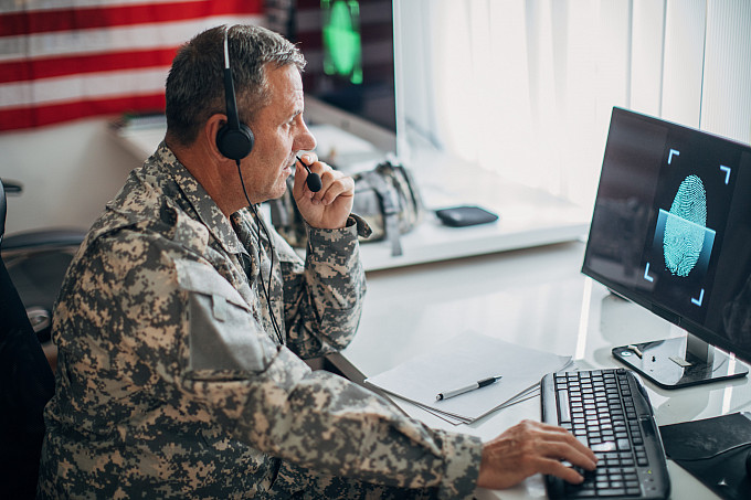 American soldier sitting in an office alone, using a computer.
