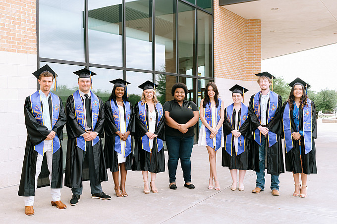 ASU graduates smiling in caps and gowns with a Delta Sigma Pi stole