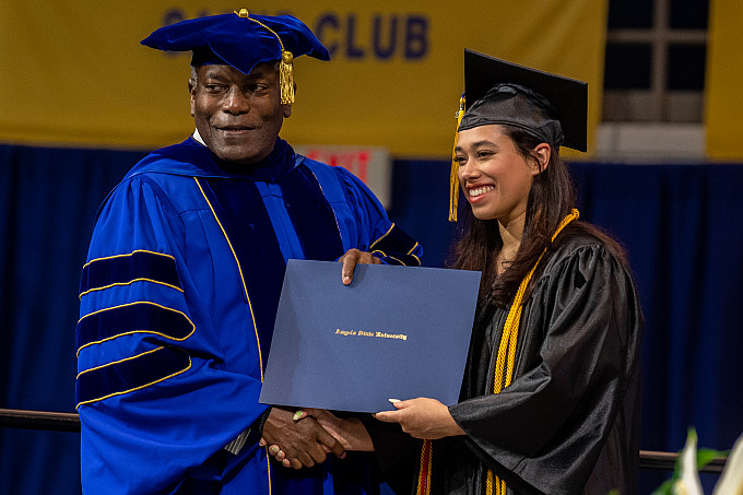 Students smiling while the President gives her the diploma at the Spring 2022 Graduation ceremony.
