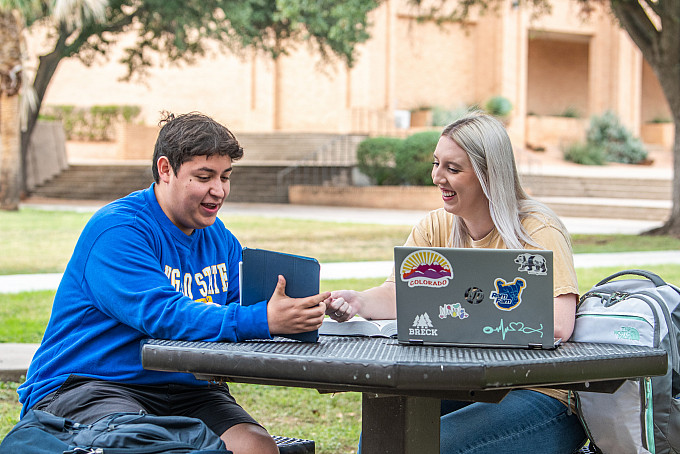 Student showing another student something on a tablet outside.