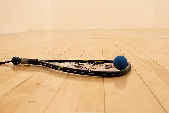 Close up of racquet and ball on racquetball court.