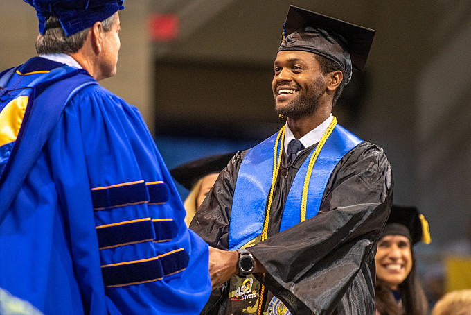 A student shaking hands with a professor on stage at graduation