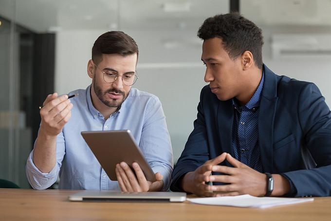 Two businessmen talking in an office while looking a tablet.