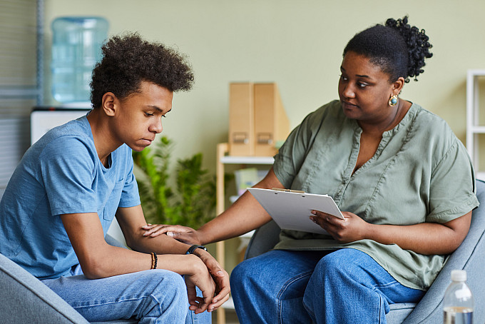 A female psychologist supporting a depressed teenage boy during a therapy session.