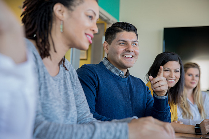 A Hispanic man leading the discussion in a staff meeting with other creative professionals at a higher education institution.