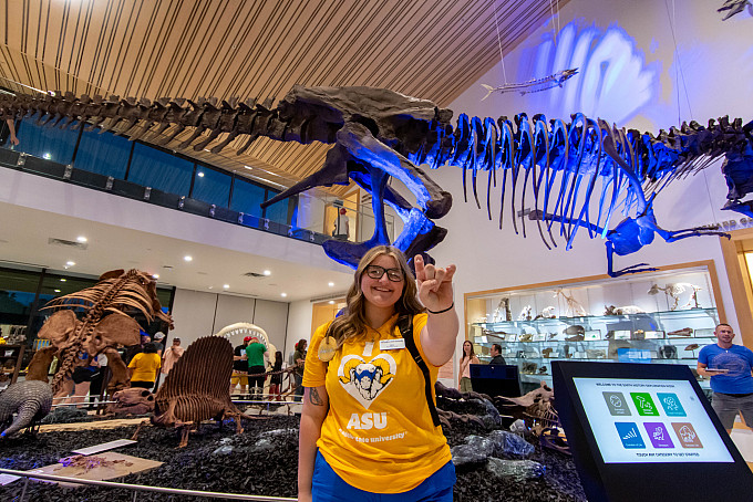 Studnet holding up the ram hand in front of a T-rex at the Mayer Museum