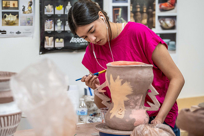 Ceramics 6655 Ceramics student listening to music while painting a clay pot.