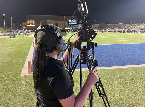 Student operating a video camera during a football game.